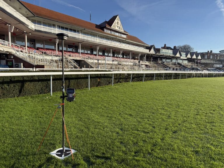 Chester Racecourse grandstand with lush green track and clear blue sky.