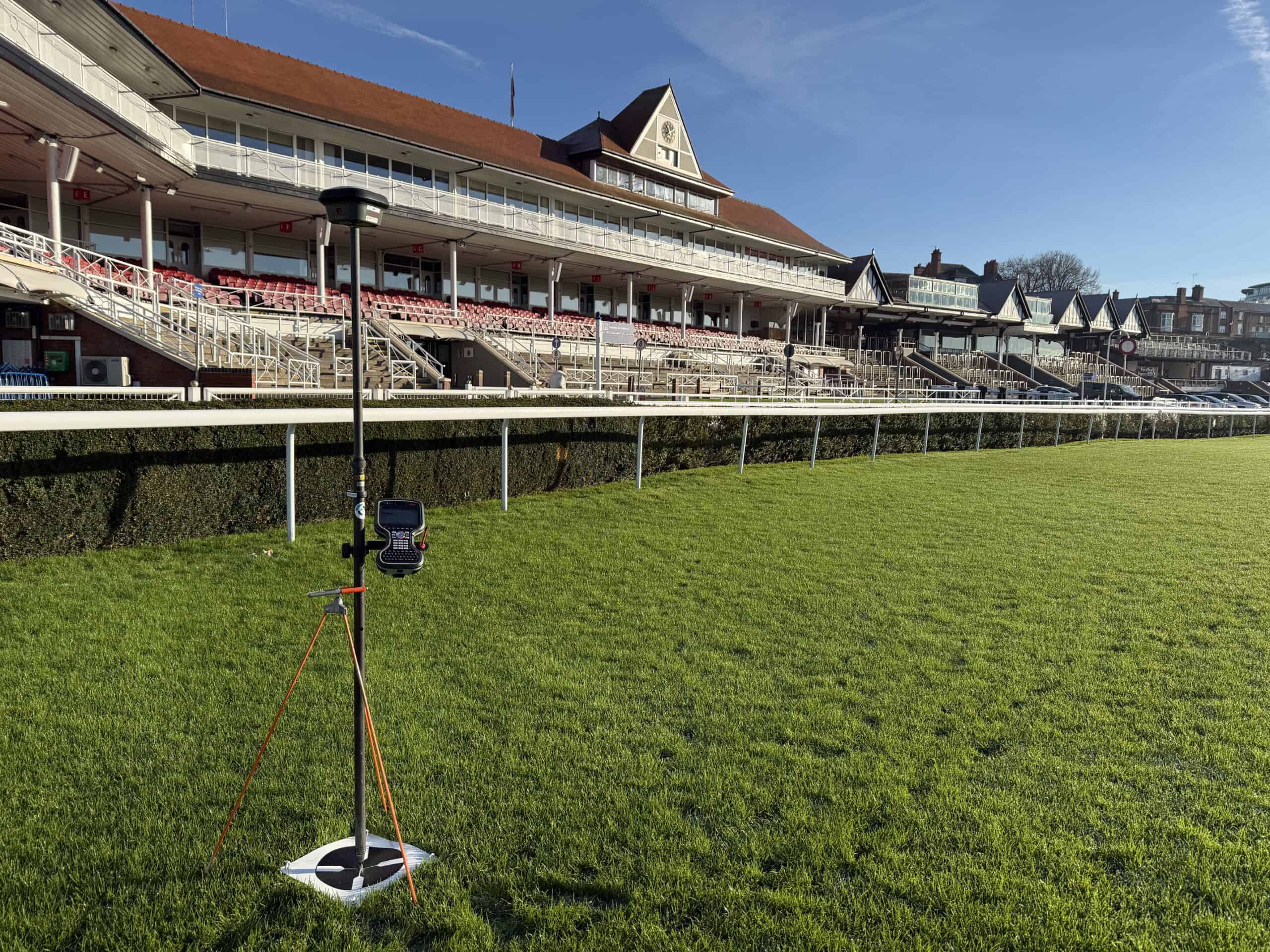 Chester Racecourse grandstand with lush green track and clear blue sky.