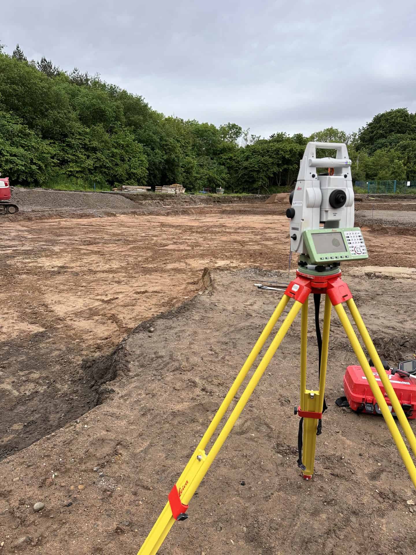 Land survey equipment on construction site with trees in background.