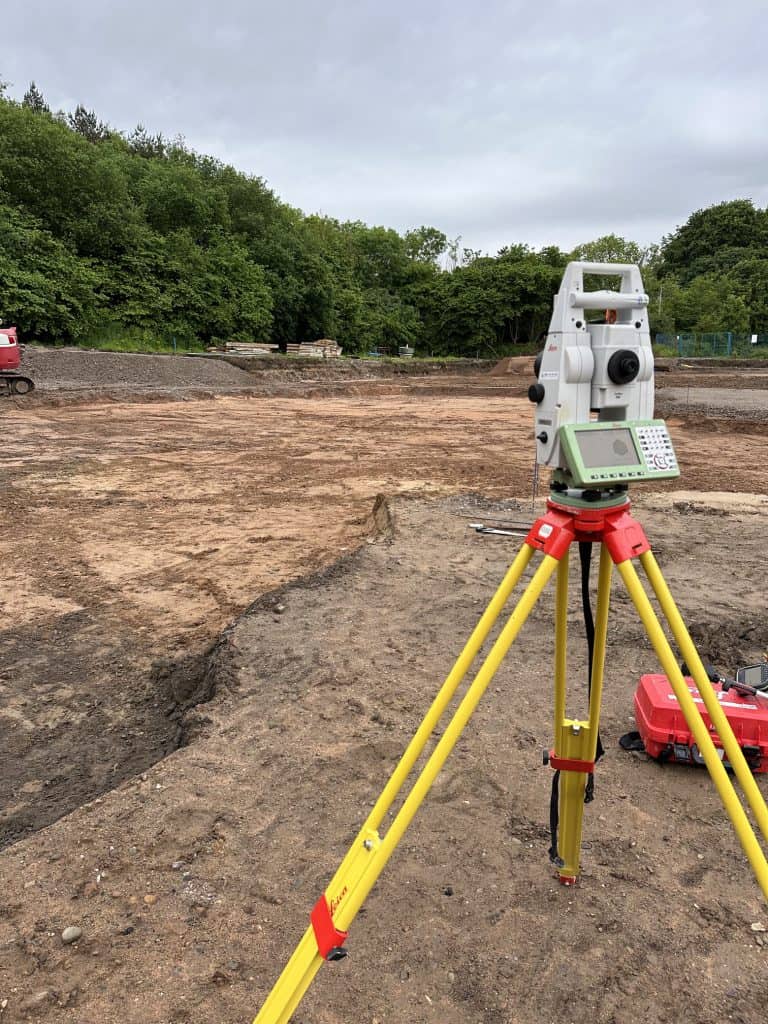 Land survey equipment on construction site with trees in background.