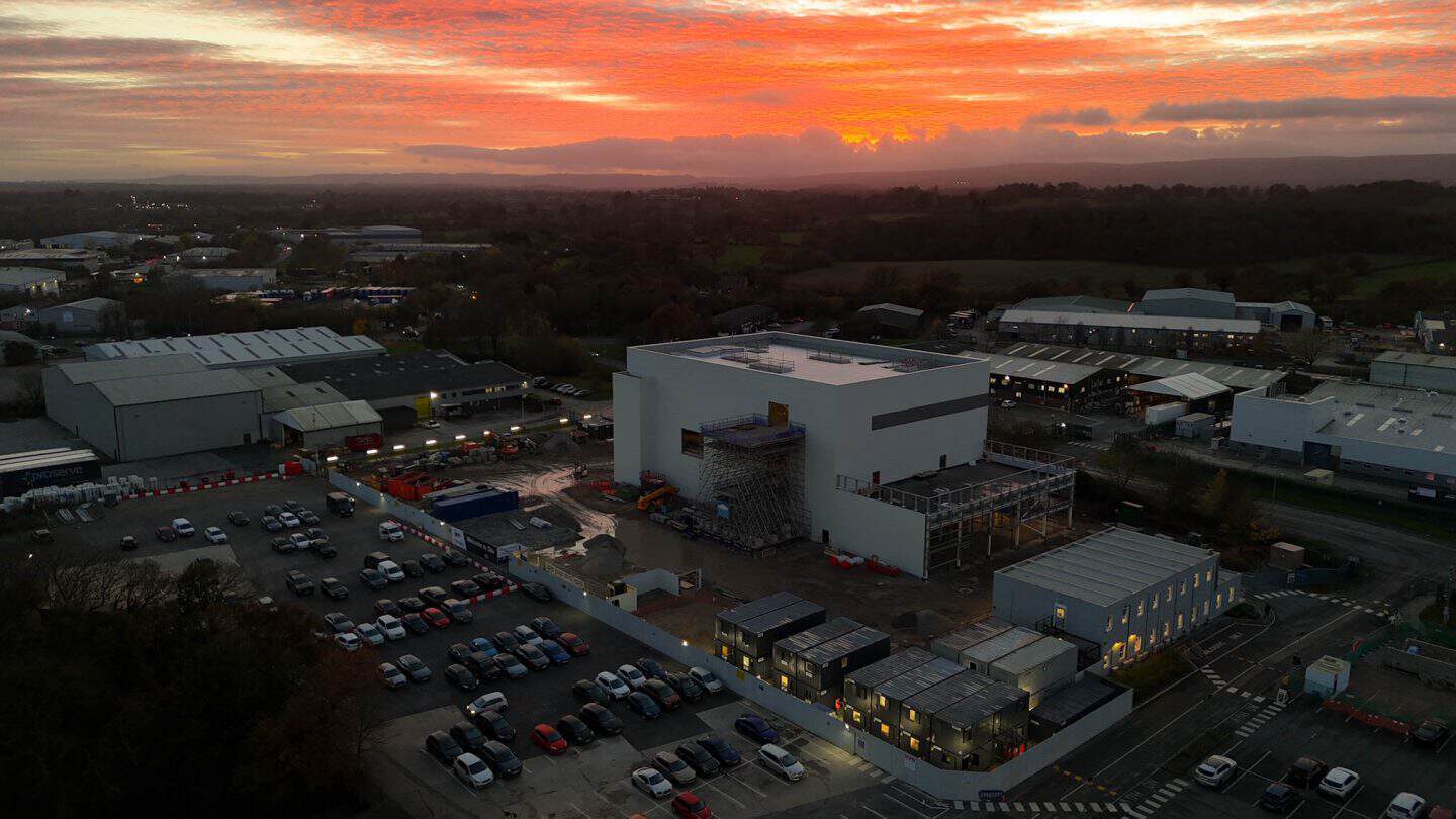Construction site at sunset with buildings and parking lot.