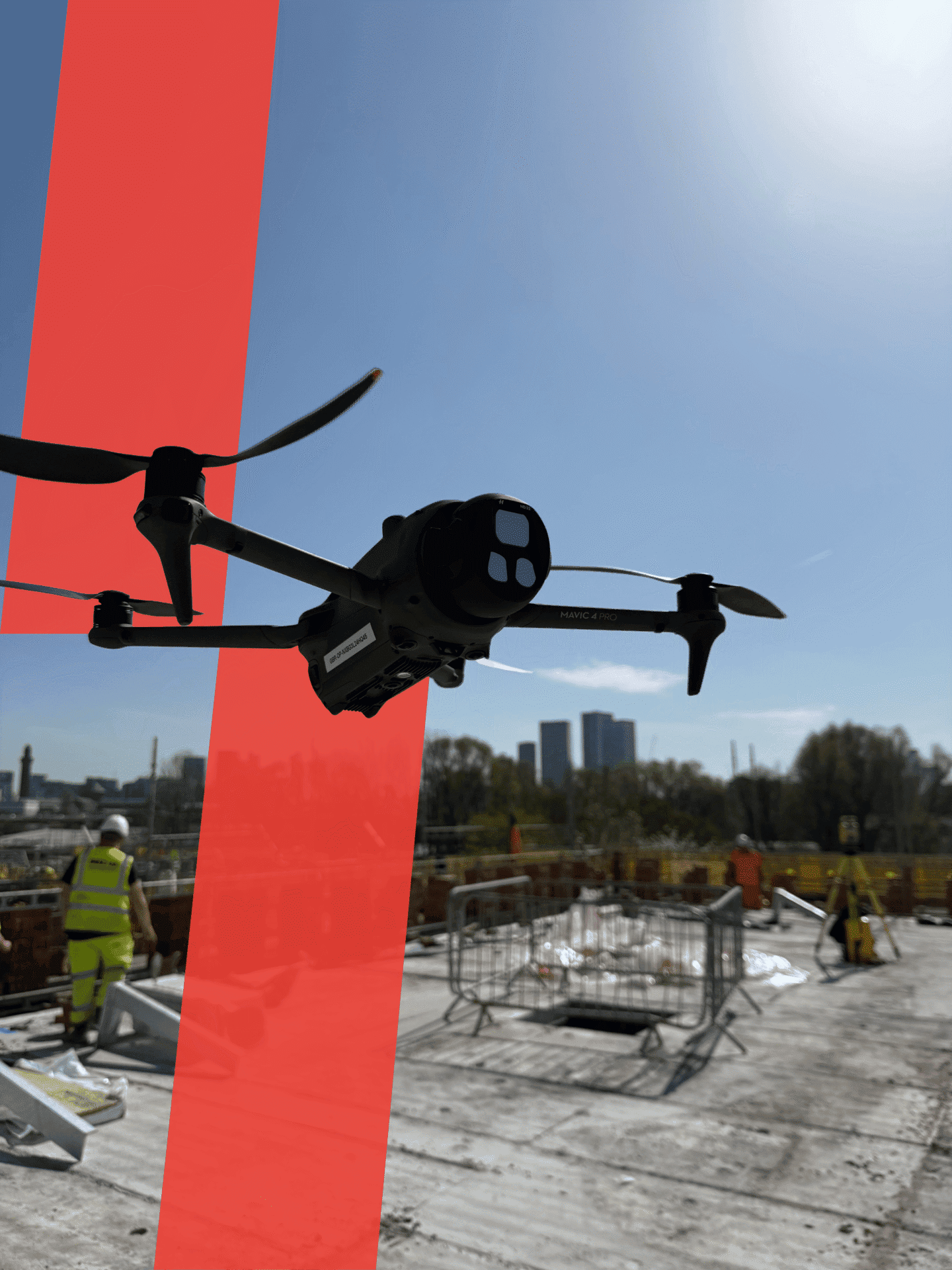 Drone flying over construction site with workers and city skyline in background.