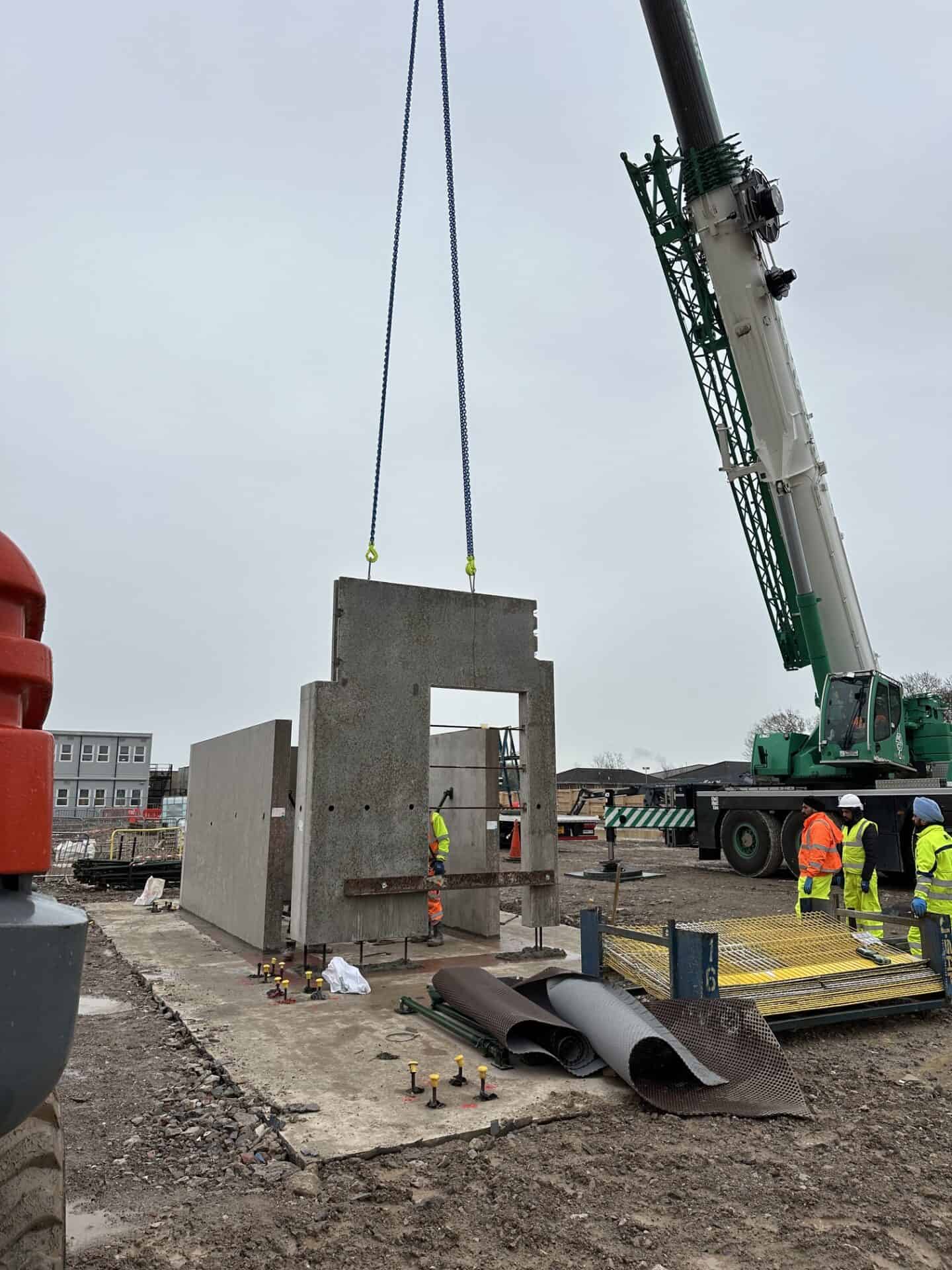 Crane lifting concrete wall panel at construction site in cloudy weather.
