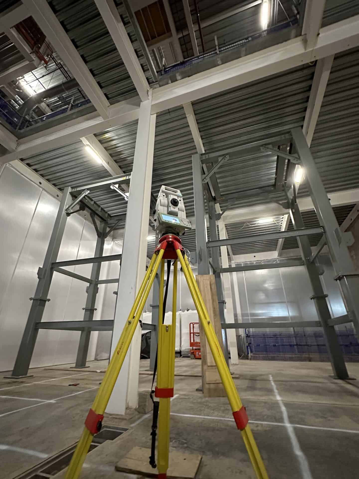 Surveying equipment on construction site with steel framework and high ceiling.