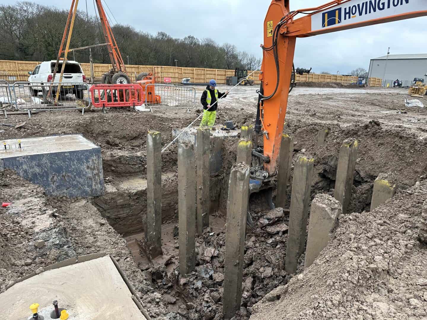 Construction site with excavator, workers, and foundation work in progress.